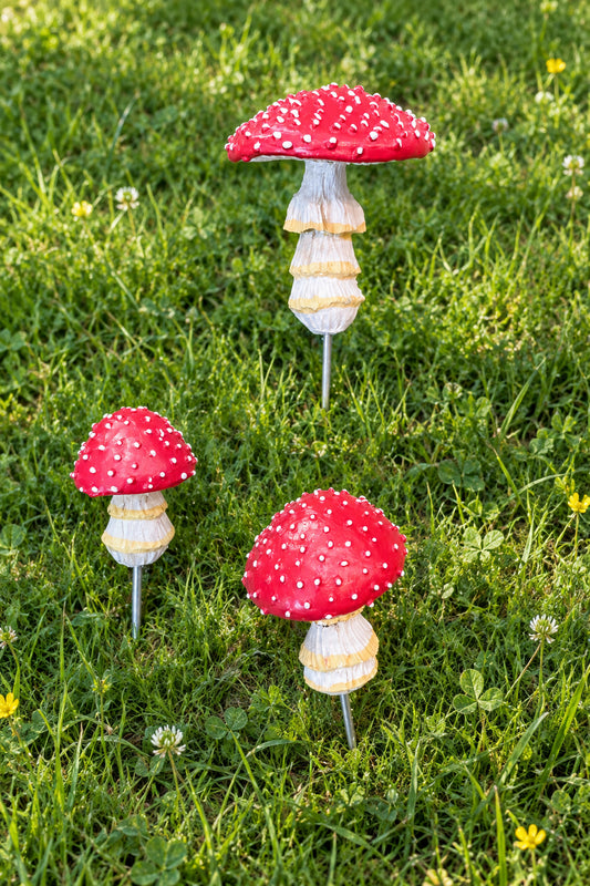 Three miniature red and white spotted mushroom figurines with striped beige and white stems, arranged on a textured brown surface.