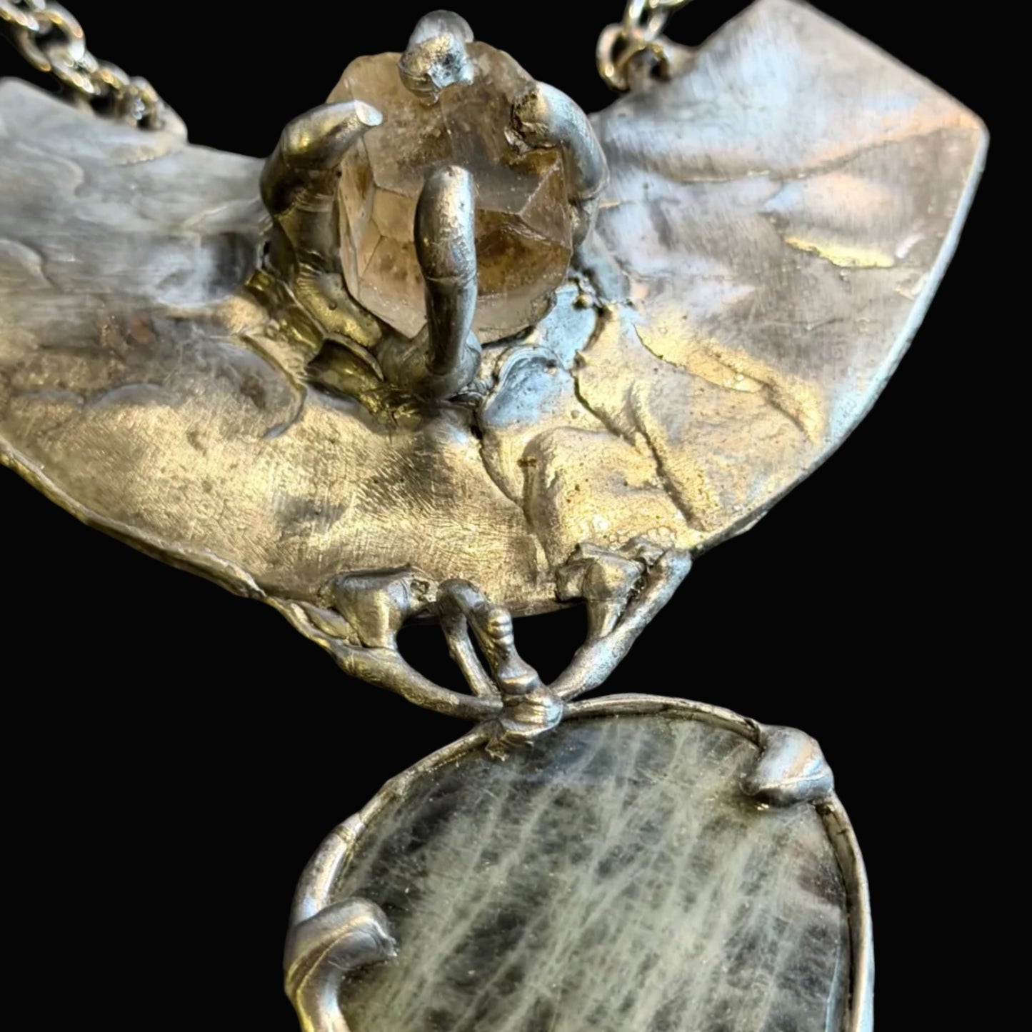 An abstract textured silver pendant necklace featuring a large sculptural top section and a teardrop-shaped clear stone pendant below, displayed on a dark textured background.