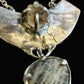 An abstract textured silver pendant necklace featuring a large sculptural top section and a teardrop-shaped clear stone pendant below, displayed on a dark textured background.