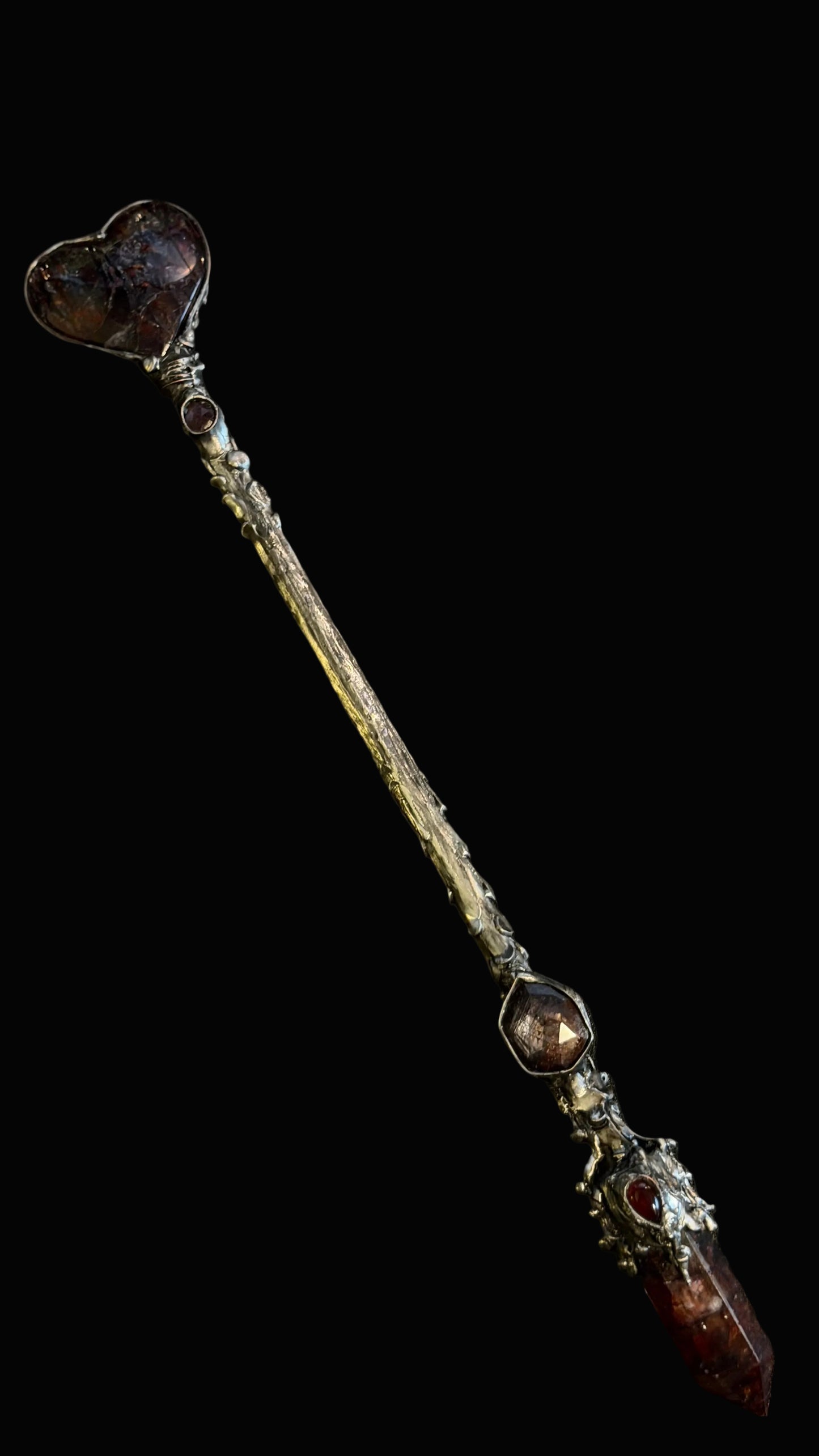A decorative wand or staff with a heart-shaped crystal top, a textured silver-toned handle, and a pointed crystal end, displayed diagonally on a dark background.