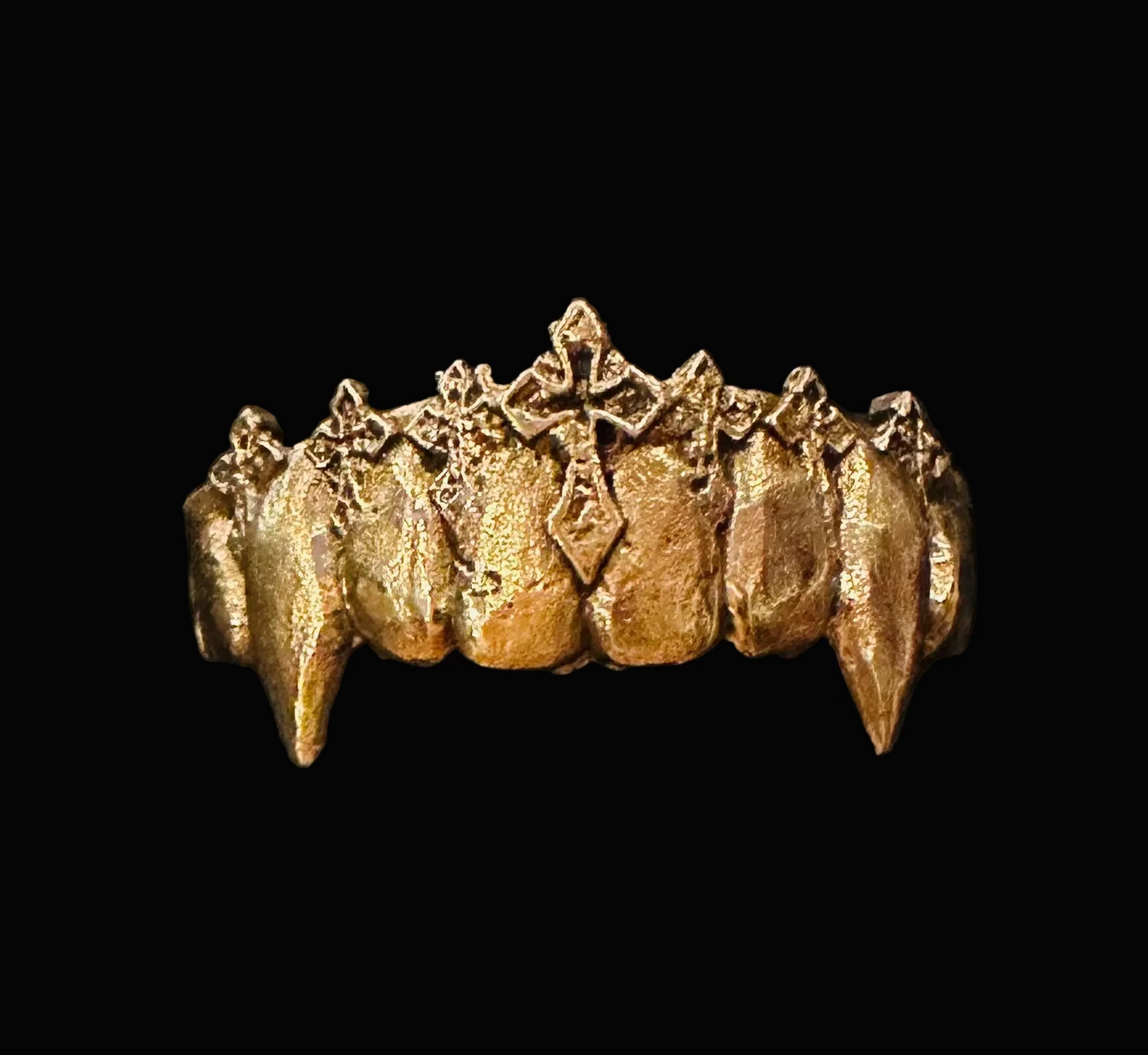 A gold-colored vampire fang grillz ring displayed in a black textured presentation box.