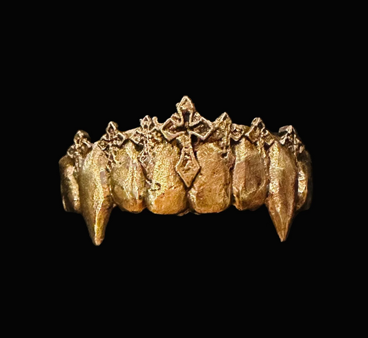 A gold-colored vampire fang grillz ring displayed in a black textured presentation box.