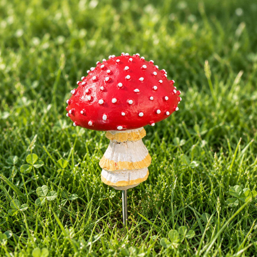 A decorative mushroom-shaped object with a red cap covered in small white dots, a beige and white striped stem, and a dark metal rod extending from the side, placed on a textured brown surface.