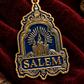 A gold and blue keychain with 'SALEM' written on it and a design that includes a tattoo art style rendering of a lantern.